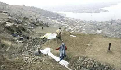  ?? — AP ?? KABUL: An Afghan man carries a bag of dirt to repair the mud roof of his house and prevent rain from leaking inside, on the outskirts of Kabul, Afghanista­n.