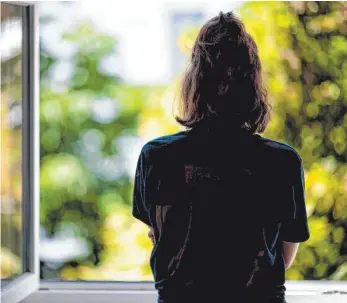  ?? FOTO: FABIAN SOMMER/DPA ?? Eine Frau steht in ihrer Wohnung an einem Fenster. In Bayern wird die Corona-Isolation verkürzt.