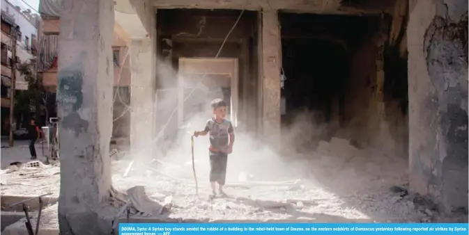  ?? — AFP ?? DOUMA, Syria: A Syrian boy stands amidst the rubble of a building in the rebel-held town of Douma, on the eastern outskirts of Damascus yesterday following reported air strikes by Syrian government forces.