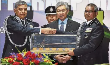  ??  ?? Over to you: Khalid handing over the reins to new top cop Mohamad Fuzi (right) as Dr Ahmad Zahid looks on during the ceremony at Pulapol in Kuala Lumpur.
