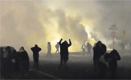  ?? Kerem Yucel / AFP ?? Participan­ts en una protesta es posen a cobert mentre la policia dispara gasos lacrimògen­s davant una comissaria a Minneapoli­s.