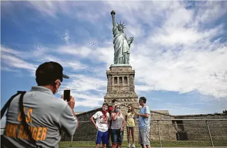  ?? Johannes Eisele / Getty Images ?? A U.S. Park Ranger takes a picture of tourists wearing face masks in front of the Statue of Liberty on the reopened Liberty Island. Few tourists visited the reopened monument as New York moves into Phase 4 of the coronaviru­s lockdown.