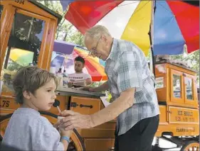  ?? Rebecca Lessner/Post-Gazette ?? Gus Kalaris, 86, of Gus and YiaYia’s cart serves an ice ball to Montgomery Nemer, 3, of Gibsonia on Friday in Allegheny Commons Park West on the North Side. Mr. Kalaris and his daughter, Christina Avalon, 62, have continued operation of the cart that...