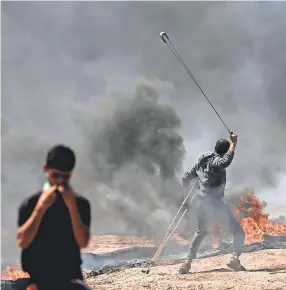  ?? KHALIL HAMRA/AFP/GETTY IMAGES ?? A Palestinia­n man whirls a slingshot during clashes with Israeli forces near the Gaza border.