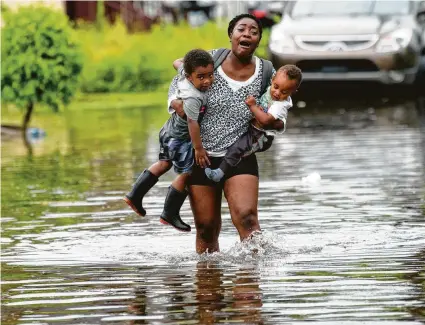  ?? Matthew Hinton / Associated Press ?? Terrian Jones carries Drew and Chance Furlough to their mother Wednesday on a flooded Belfast Street in New Orleans. A storm churning off the Gulf Coast has potential to become a tropical depression today and is expected to bring a lot of rain to Louisiana and Southeast Texas. Houston residents were stocking up on supplies, just in case.