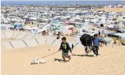  ?? /Reuters ?? Childhood denied: Children walk with a dog as displaced Palestinia­ns, who fled their houses due to Israeli strikes, take shelter in a tent camp in Rafah.