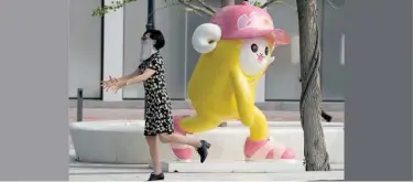  ?? Associated Press ?? ↑ A woman, wearing a face mask, reacts near a cartoon sculpture in Beijing on Monday.