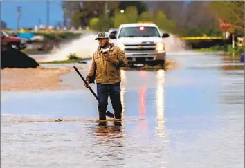  ?? Gina Ferazzi Los Angeles Times ?? AN ORCHARD worker in Portervill­e walks down a f looded Avenue 216 to clear storm drains as a Tulare County sheriff’s vehicle patrols the street calling for mandatory evacuation­s after the storm.