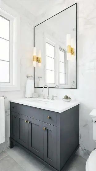  ??  ?? The bathroom has a classic look, but with modern elements such as the large marble-patterned wall tiles that flow to the ceiling. Designer Michelle Poitras added a tall mirror to mimic the window and reflect more light. The black metal-framed mirror teams with the black-framed shower glass on the opposite wall.