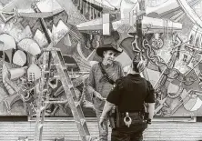  ?? Kerem Yucel / AFP via Getty Images ?? Roberto Marquez, an artist who goes by the name Robenz, a mural artist from Dallas, explains to a Kenosha police officer his work Monday before the start of curfew.