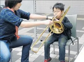 ?? Assn. of Japanese Symphony Orchestras ?? A YOUNG music student gets guidance while practicing playing the trombone.