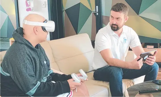  ??  ?? Damien Thompson with a patient trying a virtual reality set during a visit at Royal Brisbane and Women's Hospital.