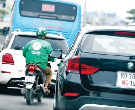  ?? ROSLAN RAHMAN/AFP ?? A Grab motorbike taxi rider plies between vehicles on a street in Hanoi on April 19.