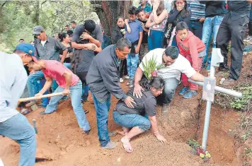  ??  ?? Mientras sus hermanos detienen la cruz con una imagen de Vladimir Oquelí, otros parientes tapan la tumba con ayuda de una pala en el cementerio municipal El Durazno.