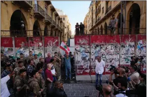  ?? (AP/Hassan Ammar) ?? A Lebanese anti-government protester holds a national Lebanese flag as a team of engineers removes a concrete wall from a road that leads to the parliament building in Beirut on Monday.