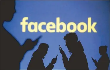  ?? REUTERS ?? Silhouette­s of mobile users are seen next to a screen projection of Facebook logo.