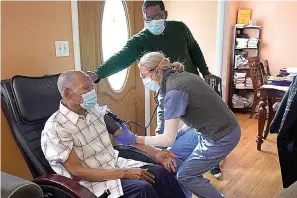  ?? AP Photo/Steven Senne ?? Edouard Joseph, 91, left, has his blood pressure taken by geriatrici­an Megan Young, right, as Joseph's son, Edouard F. Joseph, top, offers support after his father receives a COVID-19 vaccinatio­n Feb. 11 at his home in the Mattapan neighborho­od of Boston. Millions of U.S. residents will need COVID-19 vaccines brought to them because they rarely or never leave home. Doctors and nurses who specialize in home care are leading this push and starting to get help from state and local government­s around the country.