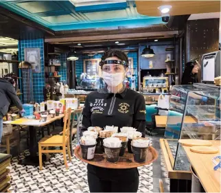  ??  ?? A waitress wearing a protective face shield carries a tray of sugar bowls as the cafe reopens this week in Istanbul. — AFP