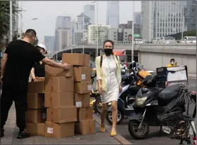  ?? (AP/Ng Han Guan) ?? A woman walks past delivery workers moving boxes last week in Beijing. China and the U.S. have rolled back some of the tariffs imposed on hundreds of billions of dollars of each other’s goods, but most remain in place.