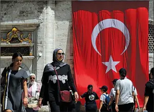  ?? AP/LEFTERIS PITARAKIS ?? People walk recently in Istanbul past a Turkish flag draping a mosque. Treasury and Finance Minister Berat Albayrak sought to calm investors’ jitters Thursday.