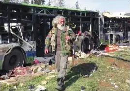  ?? AP PHOTO ?? This image from video provided by the Thiqa News Agency shows a gunman passing by buses that were damaged in a blast at the Rashideen area, a rebel-controlled district outside Aleppo city, Syria.