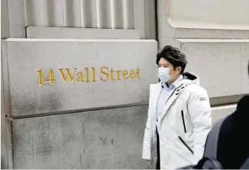  ?? — Reuters ?? A person wearing a face mask walks along Wall Street in New York City.