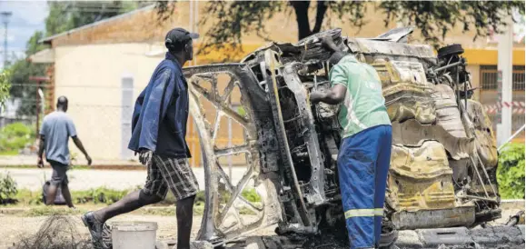  ?? (Photo: AFP) ?? BULAWAYO, Zimbabwe — Scrap metal collectors salvage sellable parts from a car shell burnt during the three-day protest in Emakhanden­i township, in Bulawayo.