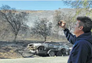  ?? Christophe­r Weber / Associated Press ?? Paul Rasmussen shoots video Monday of his burned 1968 Pontiac across from his property in Malibu. His home survived, thanks to neighbors who fought the flames with buckets and hoses.