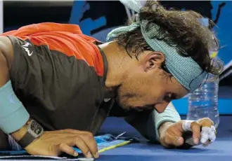  ?? Greg Wood/AFP/Getty Images ?? Rafael Nadal grimaces as a trainer works on his back Sunday between games in the men’s singles final.