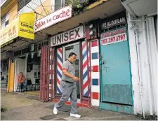  ?? XAVIER GARCIA/BLOOMBERG NEWS ?? A pedestrian passes in front of a barber shop on May 18 in San Juan, Puerto Rico. The bankruptcy of the U.S. commonweal­th and the culminatio­n of years of decline, has accelerate­d an exodus that’s adding to the island’s economic misery.