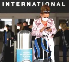  ?? — AFP photo ?? A traveller wears a face mask while checking her phone on the arrivals level outside.