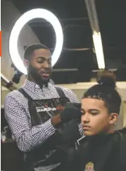  ??  ?? Greg Dixon III, left, cuts the hair of Nathan Earl, 14, at the business he runs, Legacy Barbershop, in Alton Park.
