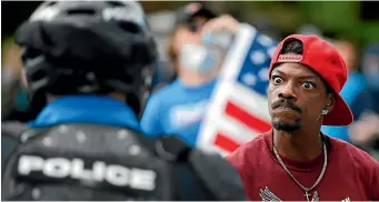  ?? AP ?? A protester stares down a Cincinnati police officer in riot gear during a march against police brutality on Saturday in Cincinnati.