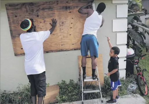  ?? Joe Raedle / Getty Images ?? Langdon Bryant and Marcus Mcclain hang plywood over the window of a home in Port Salerno, Fla., on Sunday with a little help from Torrie Bryant, age 5. Residents of Florida’s Atlantic Coast are waiting to see what path the unpredicta­ble Hurricane Dorian will take.