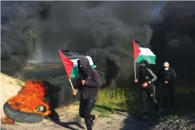  ?? AP PHOTO/ADEL HANA ?? Partly obscured by billowing smoke, protesters run along the border fence with Israel on Wednesday in Gaza City.