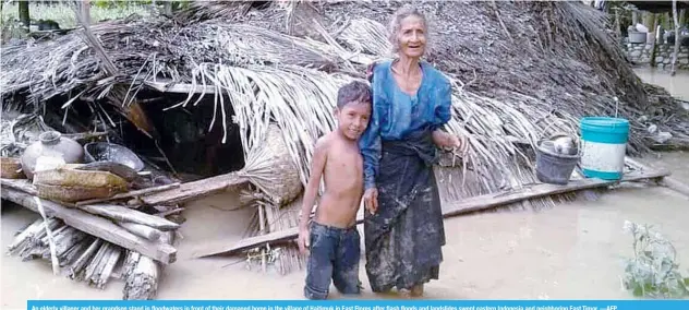  ?? —AFP ?? An elderly villager and her grandson stand in floodwater­s in front of their damaged home in the village of Haitimuk in East Flores after flash floods and landslides swept eastern Indonesia and neighborin­g East Timor.