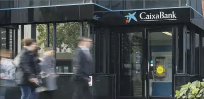  ?? ?? Un grupo de personas pasea frente a una sucursal de CaixaBank.