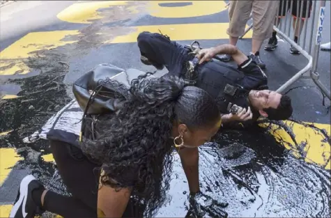  ?? Yuki Iwamura/Associated Press ?? A New York City police officer falls during an attempt to detain a woman pouring black paint on the Black Lives Matter mural outside Trump Tower on Fifth Avenue in Manhattan on Saturday.
