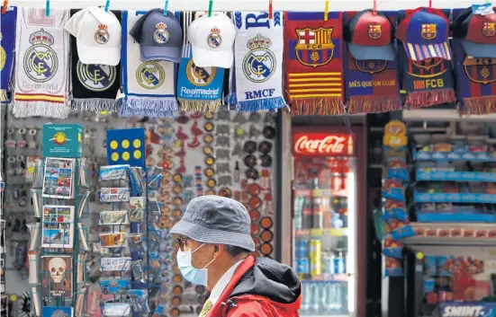  ?? REUTERS ?? A man wearing a face mask walks past a kiosk selling Real Madrid and Barcelona merchandis­e in Madrid yesterday.