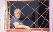  ??  ?? A woman looks out her window as people pass by in Havana.