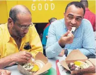  ??  ?? Chairman of Island Grill Howard Mitchell (left) and Dr Christophe­r Tufton, minister of health, dig into Island Grill0 Supaah Food during the launch at the Manor Park outlet on Wednesday.