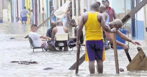  ?? AP ?? In this September 10, 2017, photo, men play dominoes in the middle of a flooded street as others pull broken furniture from calf-high water in the aftermath Hurricane Irma, in Havana, Cuba.