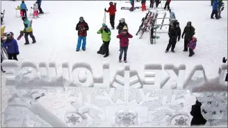  ?? Canadian Press photo ?? Tourists photograph an ice sculpture as heavy snow falls at the Lake Louise ski resort delaying the start of the women's World Cup super-G ski race at Lake Louise, Alta in 2016. The winter holidays can be an expensive time to travel for many Canadians, but with some planning it's possible not to break the bank.