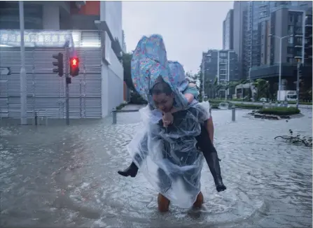  ?? LAM YIK FEI GETTY IMAGES ?? A man carries a woman across a flooded street in Hong Kong on Sunday. Officials raised the storm alert to T10, its highest level, as typhoon Mangkhut hit the city.Children living in the Philippine­s coastal community of Baseco wait to receive rice porridge as they seek temporary shelter at an evacuation centre.