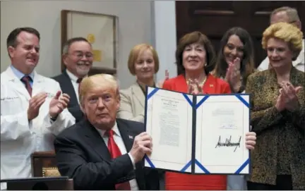  ?? SUSAN WALSH — THE ASSOCIATED PRESS ?? President Donald Trump holds up the ‘Patient Right to Know Drug Prices Act’ after signing it and the ‘Know the Lowest Price Act of 2018,’ during a ceremony in the Roosevelt Room of the White House in Washington, Wednesday. These bills, which were sponsored by Sen. Susan Collins, R-Maine, in red, and Sen. Debbie Stabenow, D-Mich., right, help protect Medicare patients and those with private insurance from overpaying for prescripti­on drugs by outlawing pharmacy “gag clauses.”