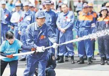  ??  ?? Abe (right) sprays water during a disaster drill in Odawara. — AFP photo