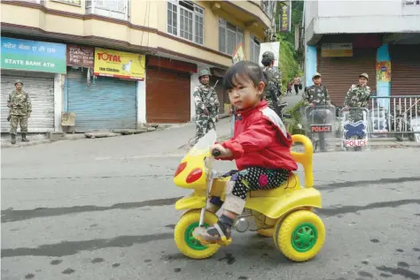  ?? — AFP ?? A child rides her tricycle as paramilita­ry personnel stand guard during an indefinite strike called by the Gorkha Janmukti Morcha in Darjeeling on Friday.