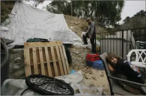  ??  ?? Andrew Joos-Visconti works to protect his back yard from the upcoming rains with a plastic tarp, in the Sun Valley area of Los Angeles on Tuesday. At right, is his daughter, Scarlett, 4. Authoritie­s ordered tens of thousands of people to flee their...