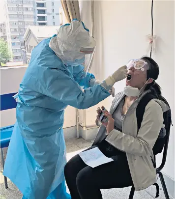  ??  ?? Sophia Yan is pictured getting disinfecte­d in the hotel lobby and, main picture, having a swab test to determine if she is infected. Left, plain clothes security officers at the cemetery