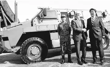  ??  ?? Turnbull (centre) shakes hands with Abe in front of a Bushmaster military vehicle at Narashino exercise field in Funabashi, east of Tokyo, Japan. — Reuters photo